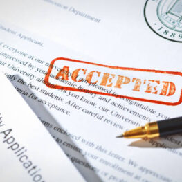 +++NOTE TO INSPECTOR +++ The letterhead and logo is a generic prop designed by me. 

Desktop still life of an accepted university application with an acceptance letter and rubber stamp of ACCEPTED.
